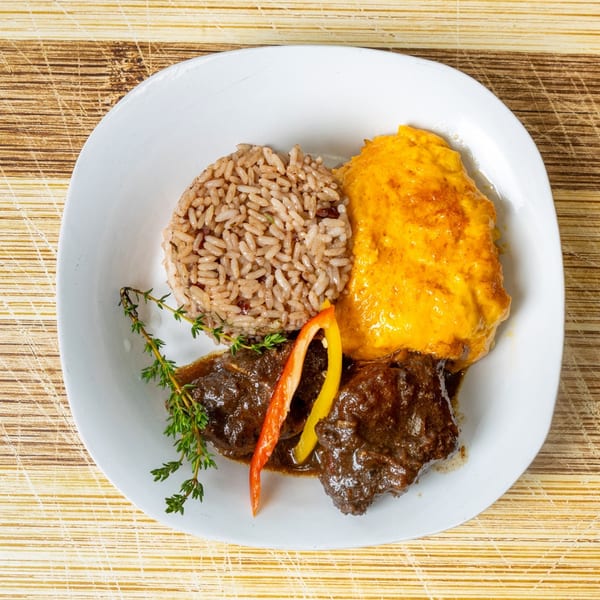 A white plate with brown rice, yellow mashed sweet potatoes, and stewed meat with herbs.