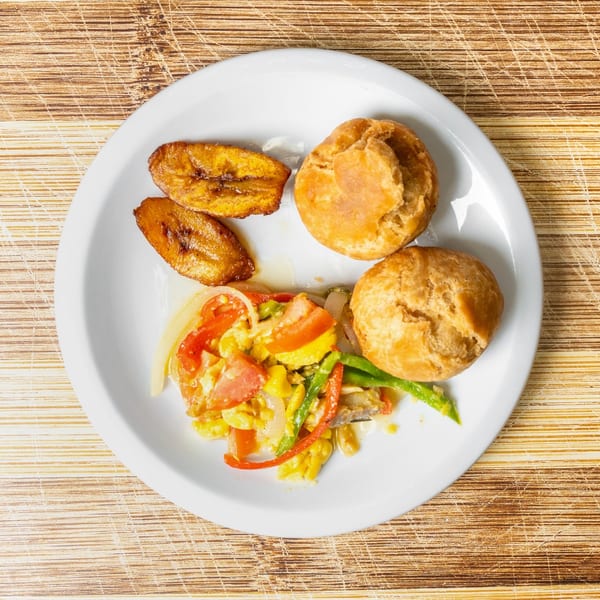 A white plate with fried plantains, two johnny cakes, and ackee and saltfish.