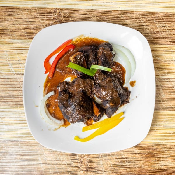 Braised oxtail in gravy with sliced red and yellow bell peppers, and white onions.